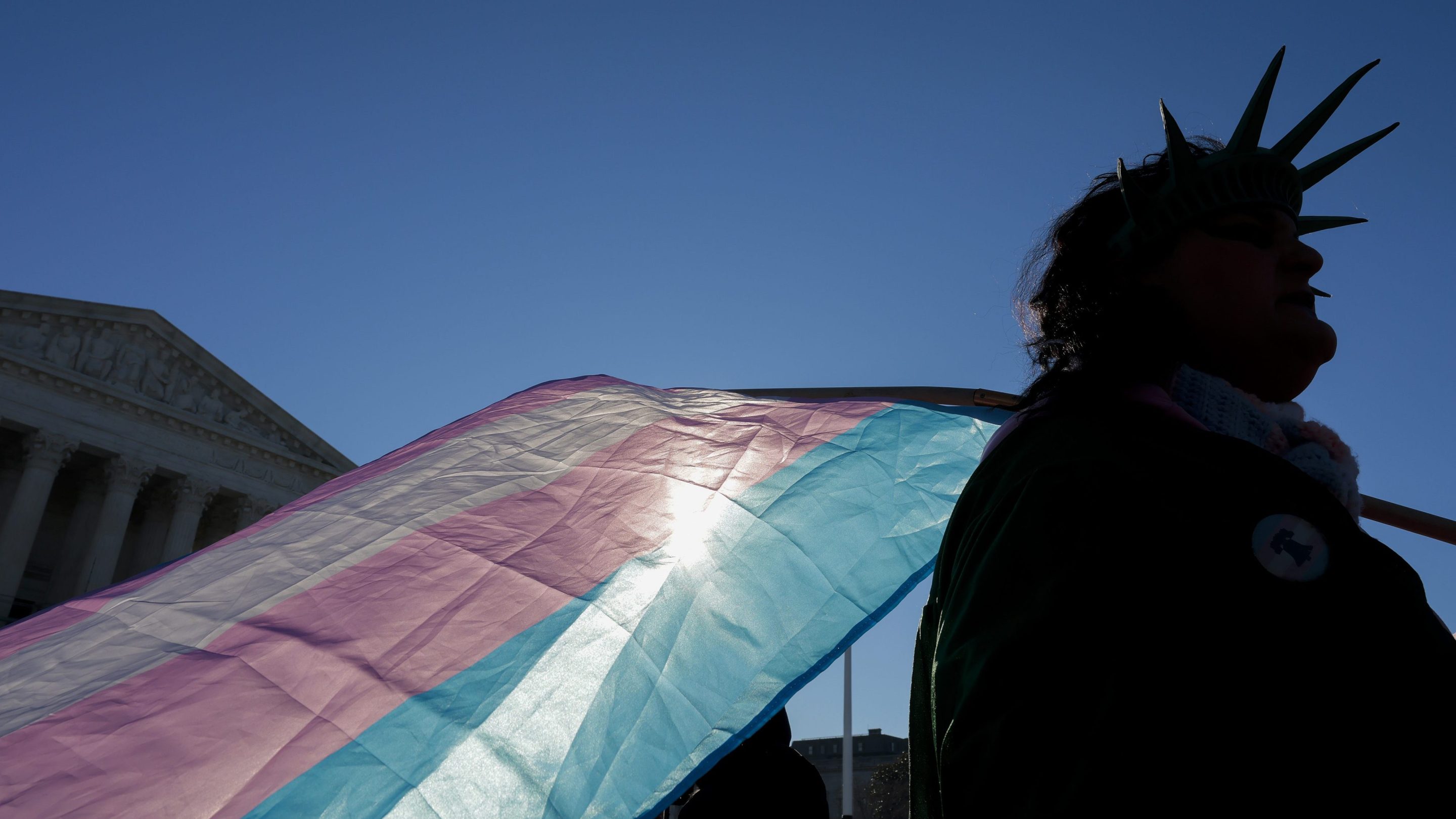 A protester supporting transgender athletes competing in women's sports holds a transgender pride flag outside the Supreme Court on January 13, 2026 in Washington, DC. The protestor is wearing a crown similar to the Statue of Liberty.