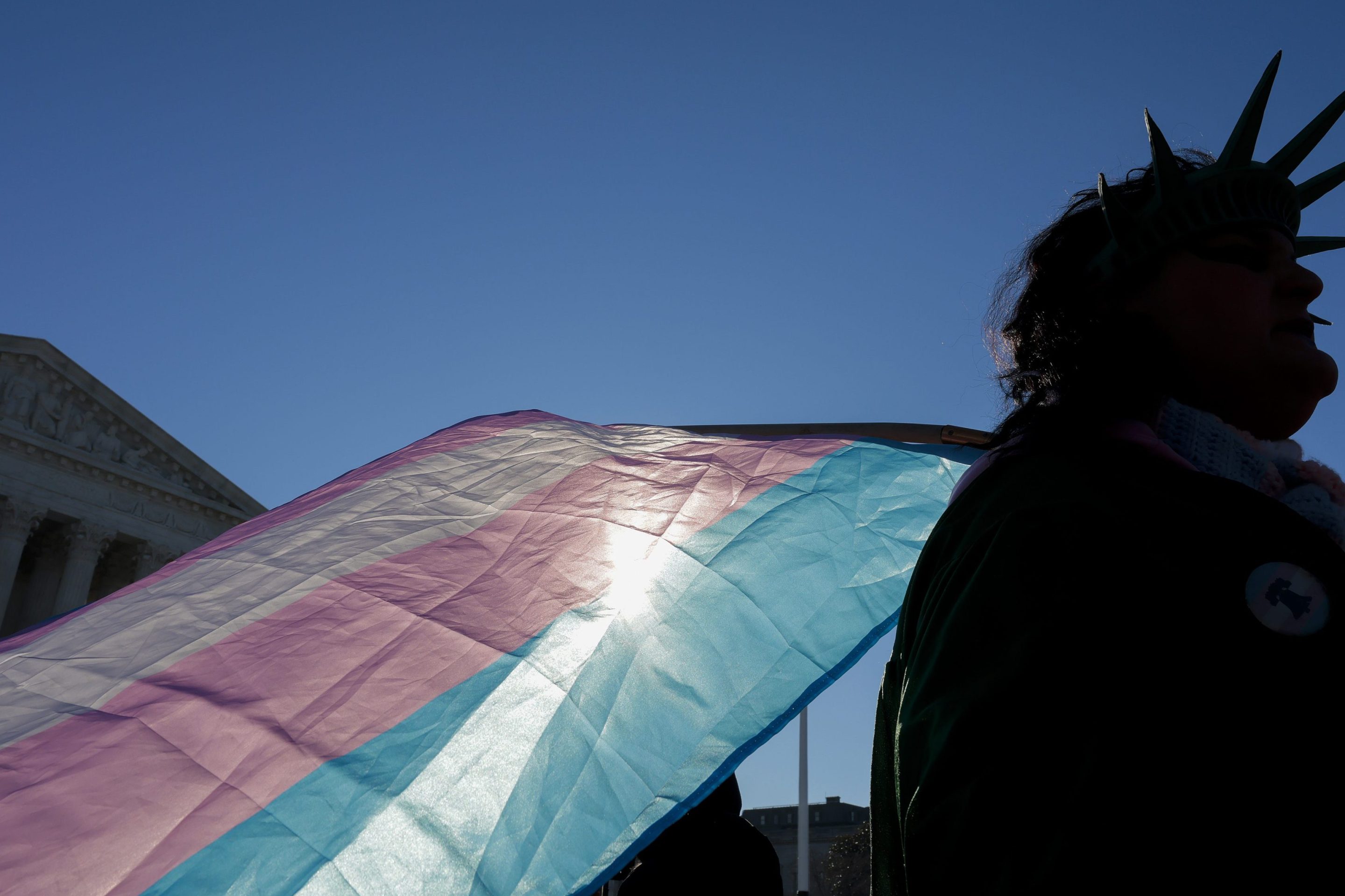 A protester supporting transgender athletes competing in women's sports holds a transgender pride flag outside the Supreme Court on January 13, 2026 in Washington, DC. The protestor is wearing a crown similar to the Statue of Liberty.