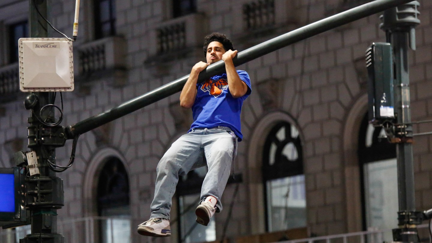 Knicks fans hang off traffic light poles as they celebrate after the New York Knicks defeated the San Antonio Spurs in Game 5 of the NBA Finals to win the series, in New York, on June 14, 2026. The Knicks won the NBA Championship for the first time since 1973, for the third time in franchise history. (Photo by )