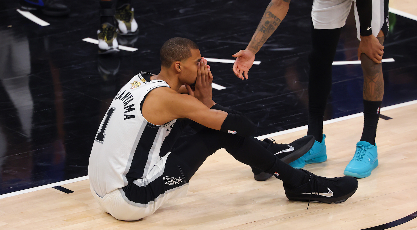 Victor Wembanyama sitting dejectedly on the floor with his hands over his face during a stoppage in play in the fourth quarter against the New York Knicks in Game Five of the 2026 NBA Finals on June 13, 2026 in San Antonio, Texas.