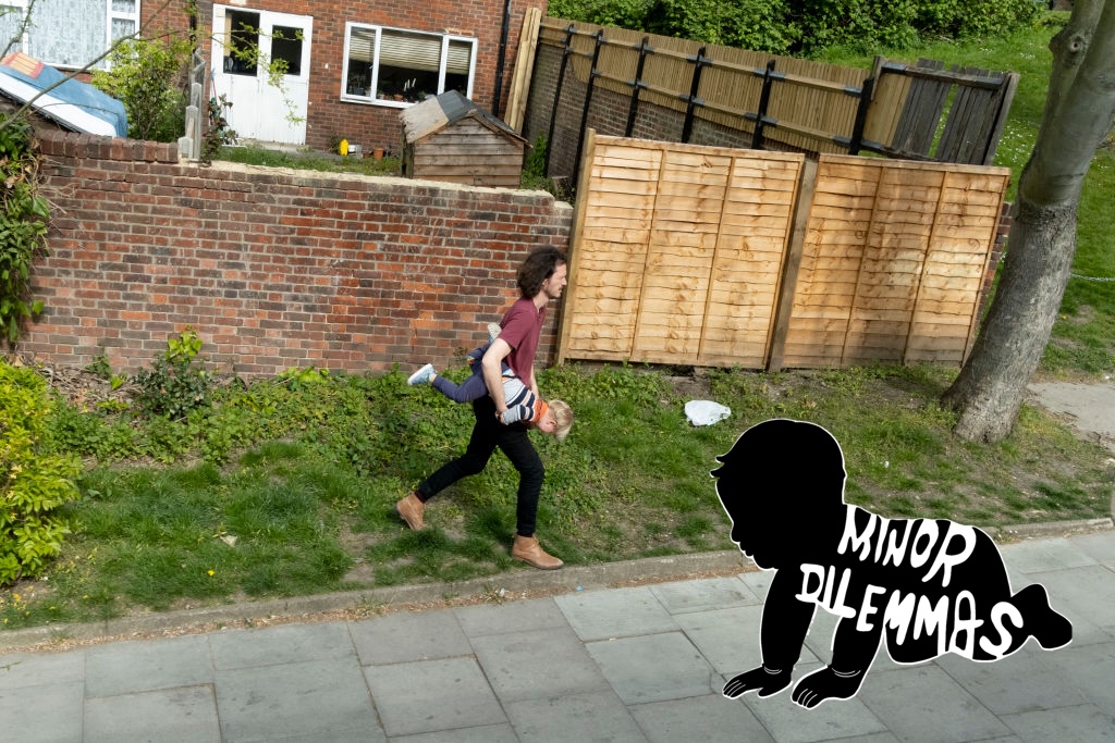 A man carries his child sideways in his arms as he walks up a road
