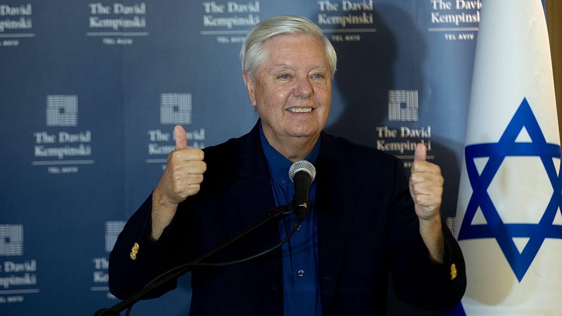 Lindsey Graham gives a double thumbs up in front of an Israeli flag