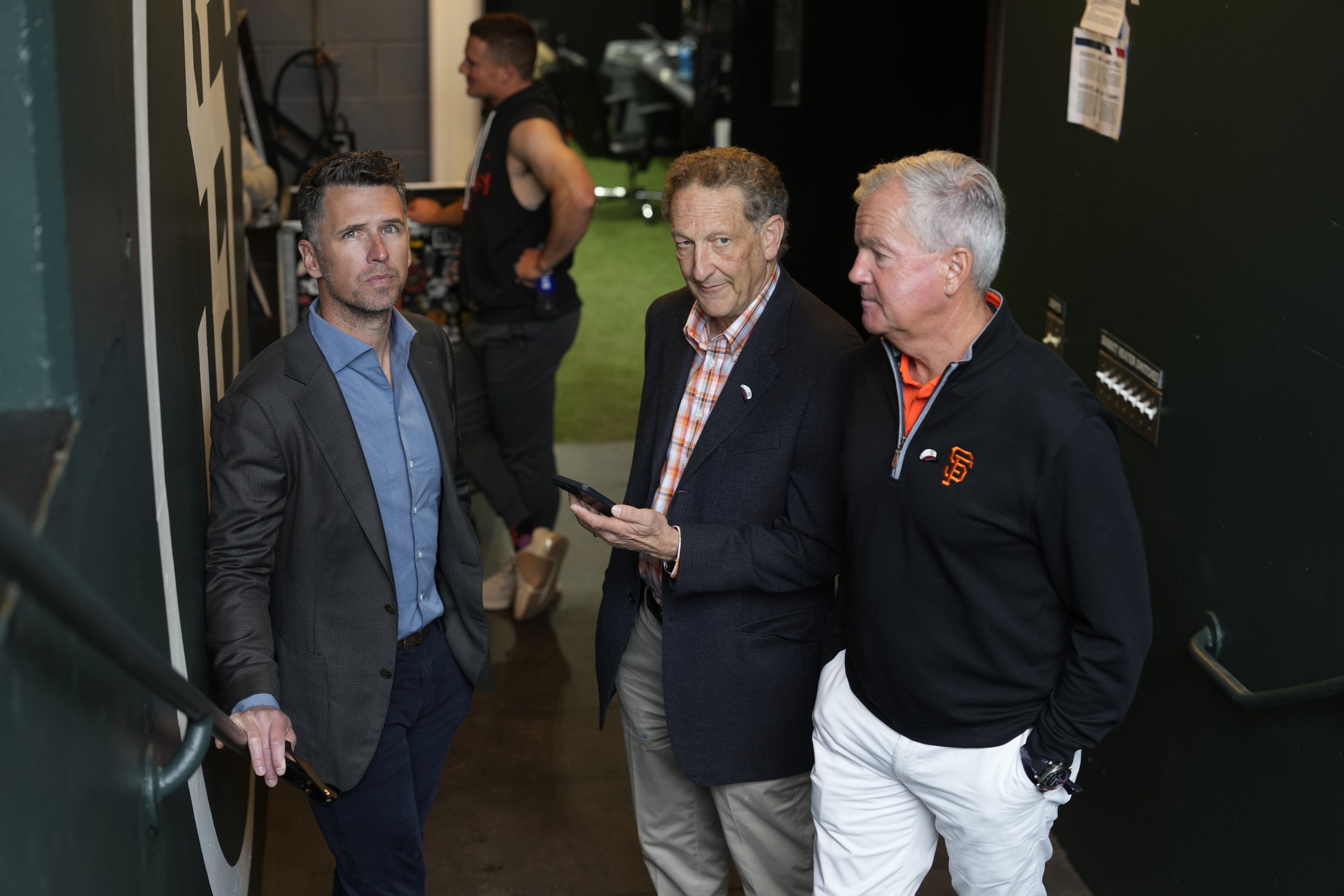 Buster Posey, Larry Baer, and Greg Johnson huddle together.