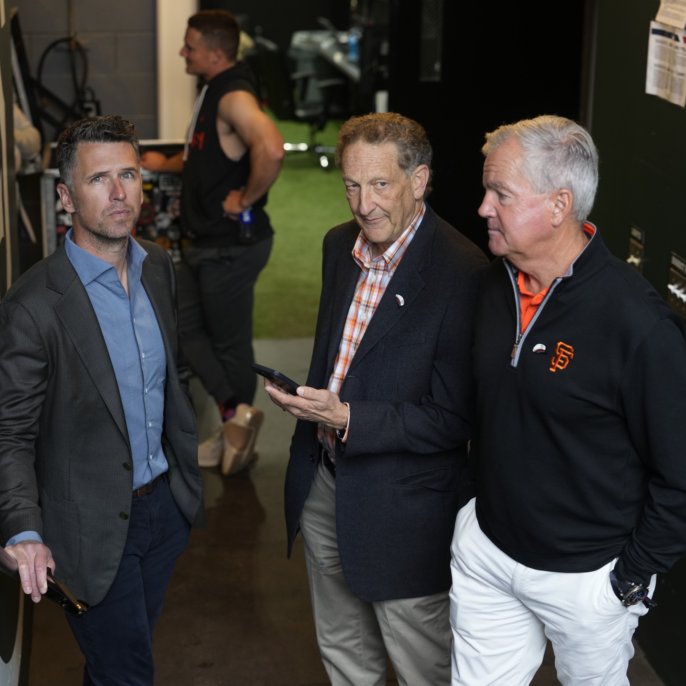 Buster Posey, Larry Baer, and Greg Johnson huddle together.