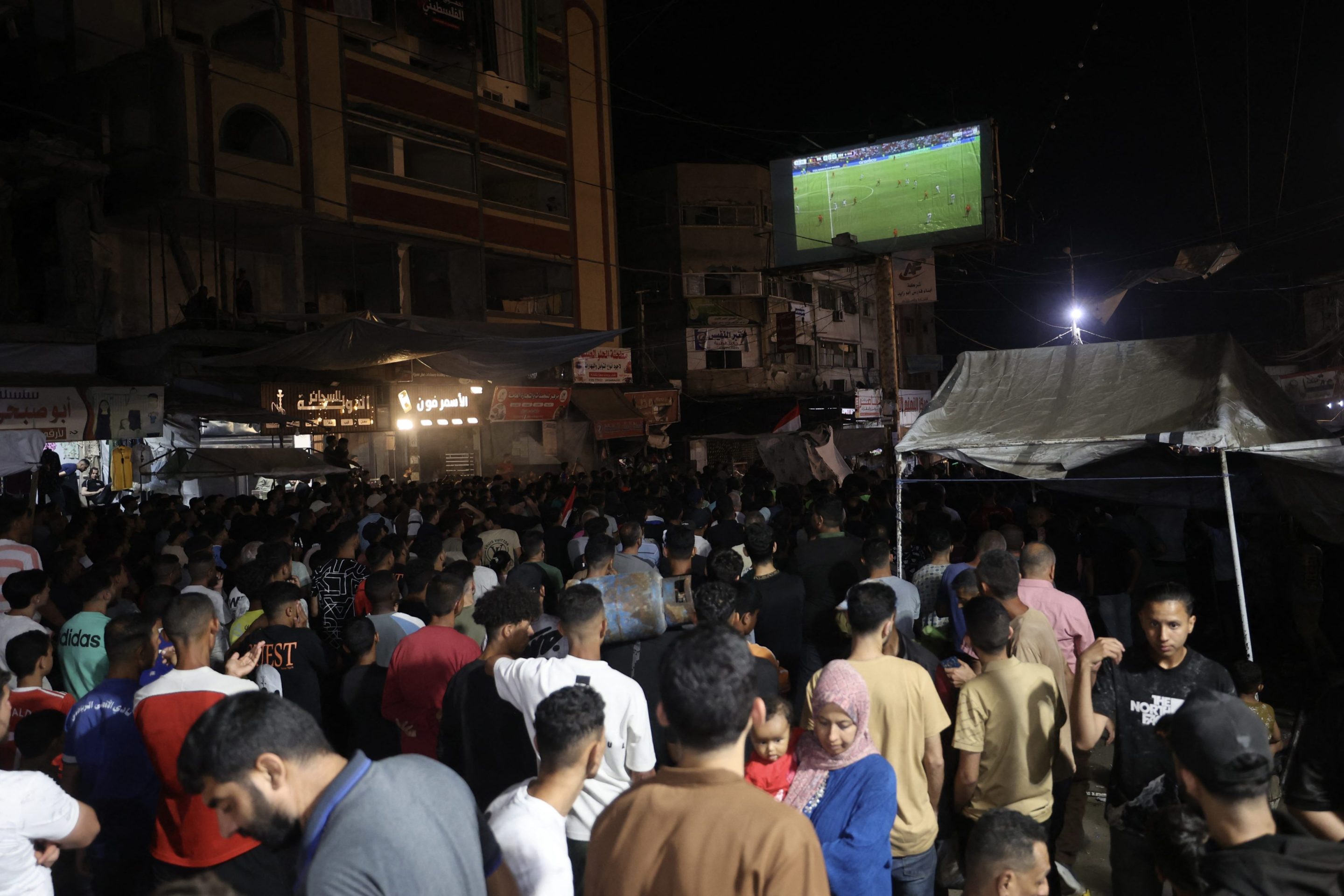 Palestinian football fans displaced from their homes, which were destroyed by Israeli military strikes, watch Belgium vs. Egypt on a giant screen at the Nuseirat refugee camp in Gaza.