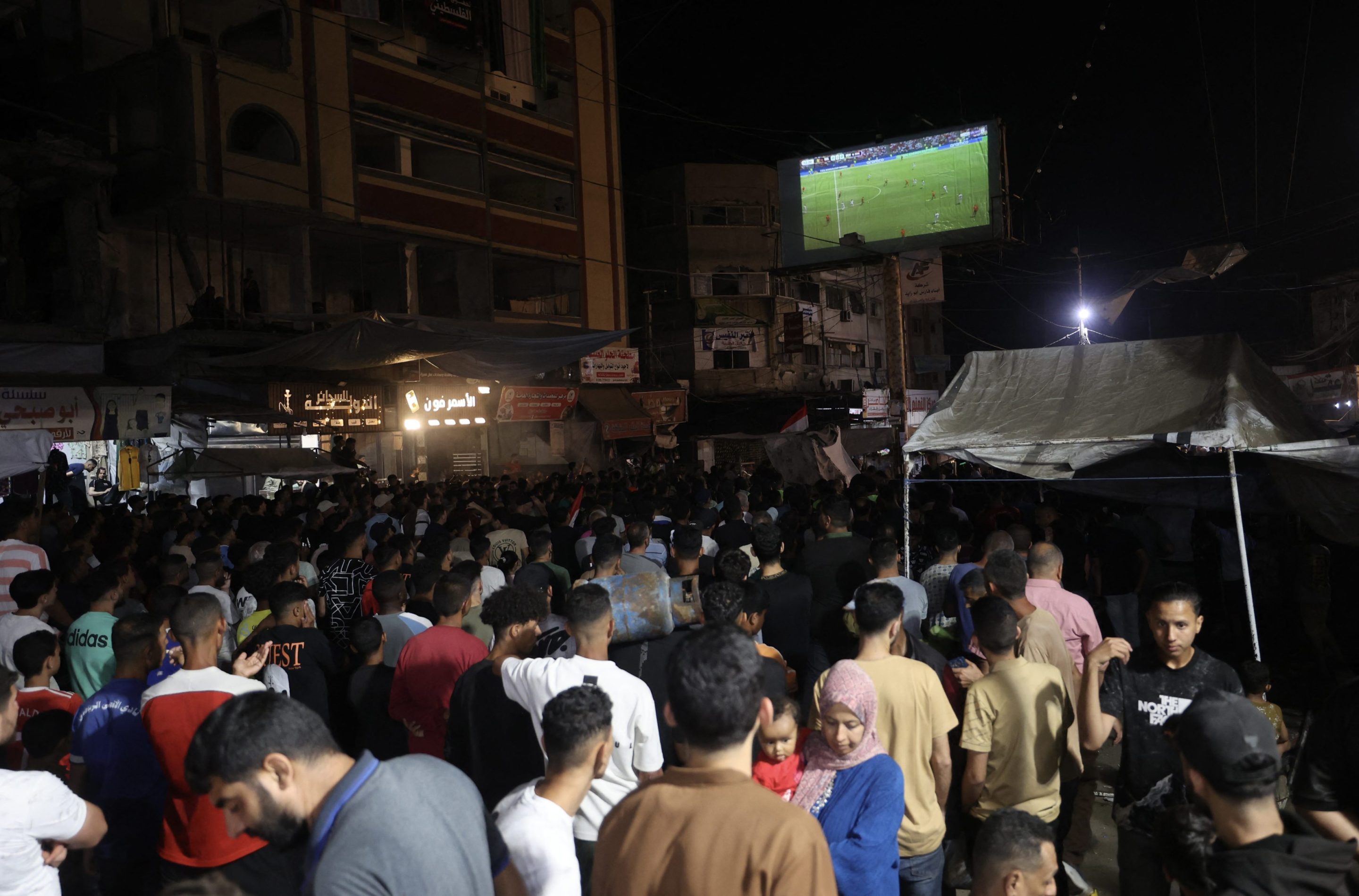 Palestinian football fans displaced from their homes, which were destroyed by Israeli military strikes, watch Belgium vs. Egypt on a giant screen at the Nuseirat refugee camp in Gaza.