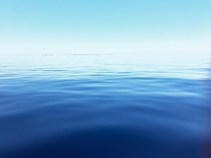 The sea is flat and glassy, with land barely visible on the horizon.