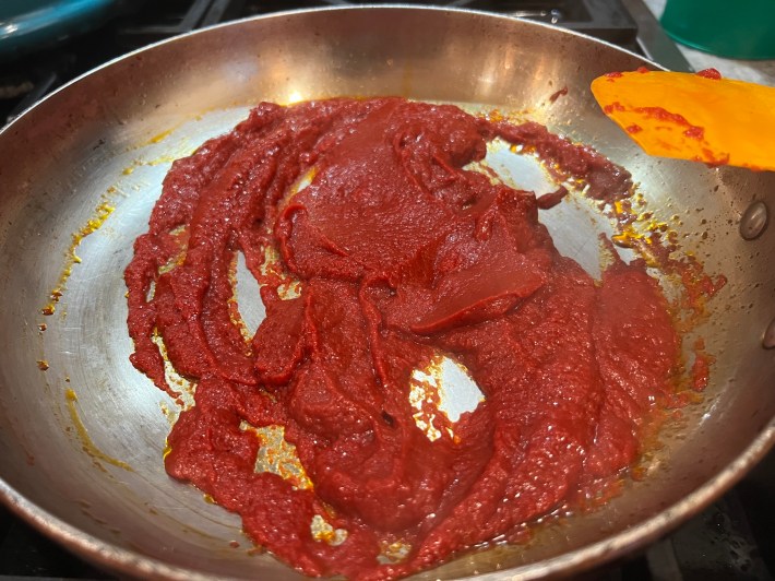 Tomato paste sizzles in a fry pan.