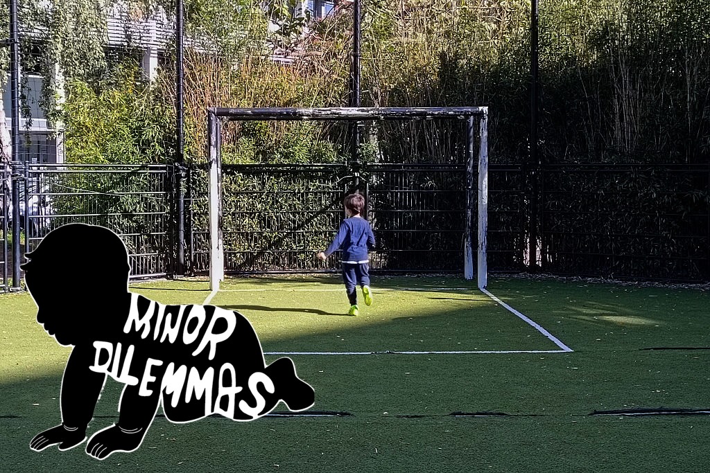 A child plays alone in a soccer goal on a grassy field