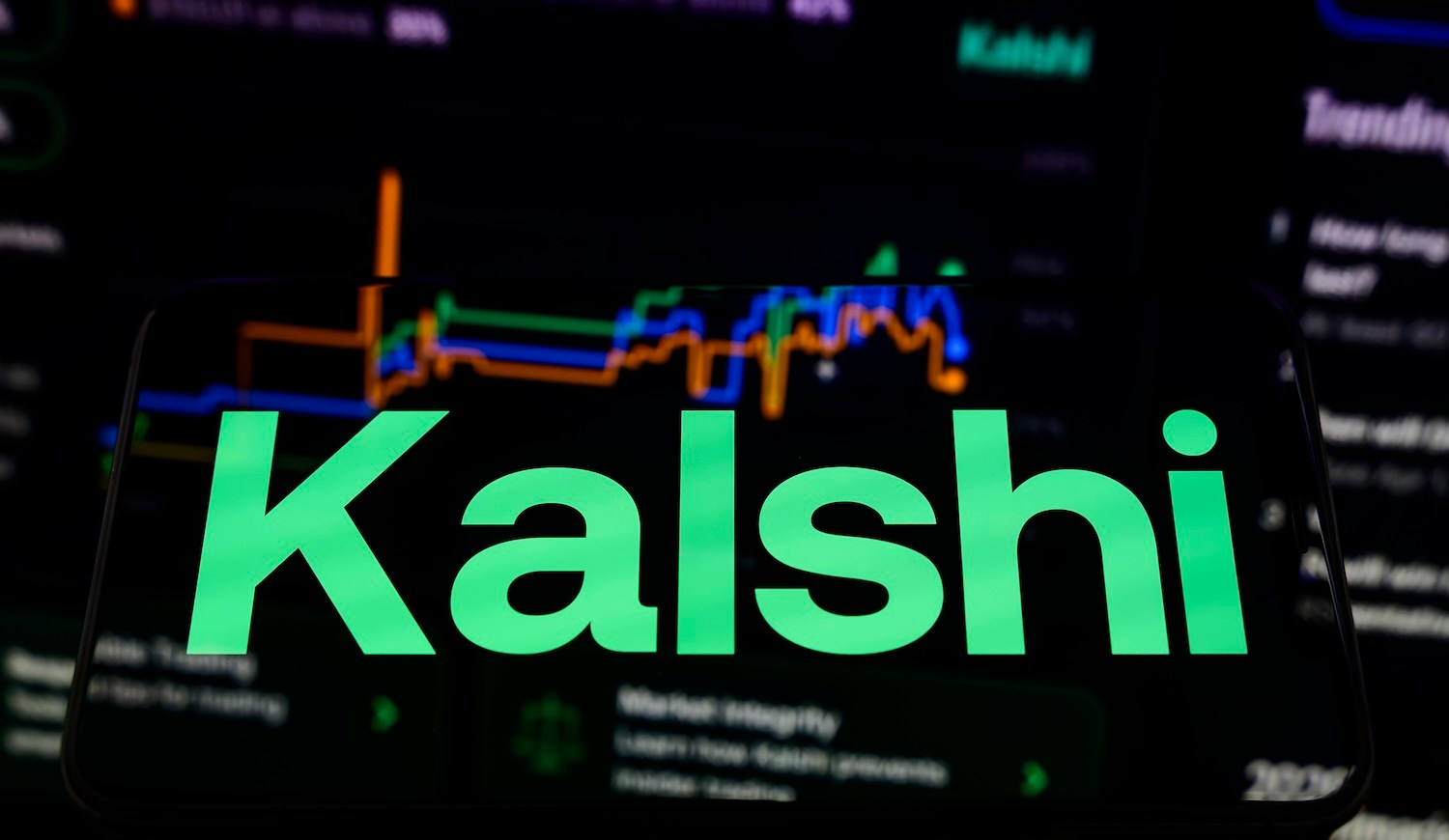 Kalshi's logo appears on a smartphone placed on a reflective surface, with a blurry betting curve projected in the background in Creteil, France, on March 9, 2026, during a major scandal and $54 million lawsuit concerning bets related to recent strikes in Iran. (Photo by Samuel Boivin/NurPhoto via Getty Images)