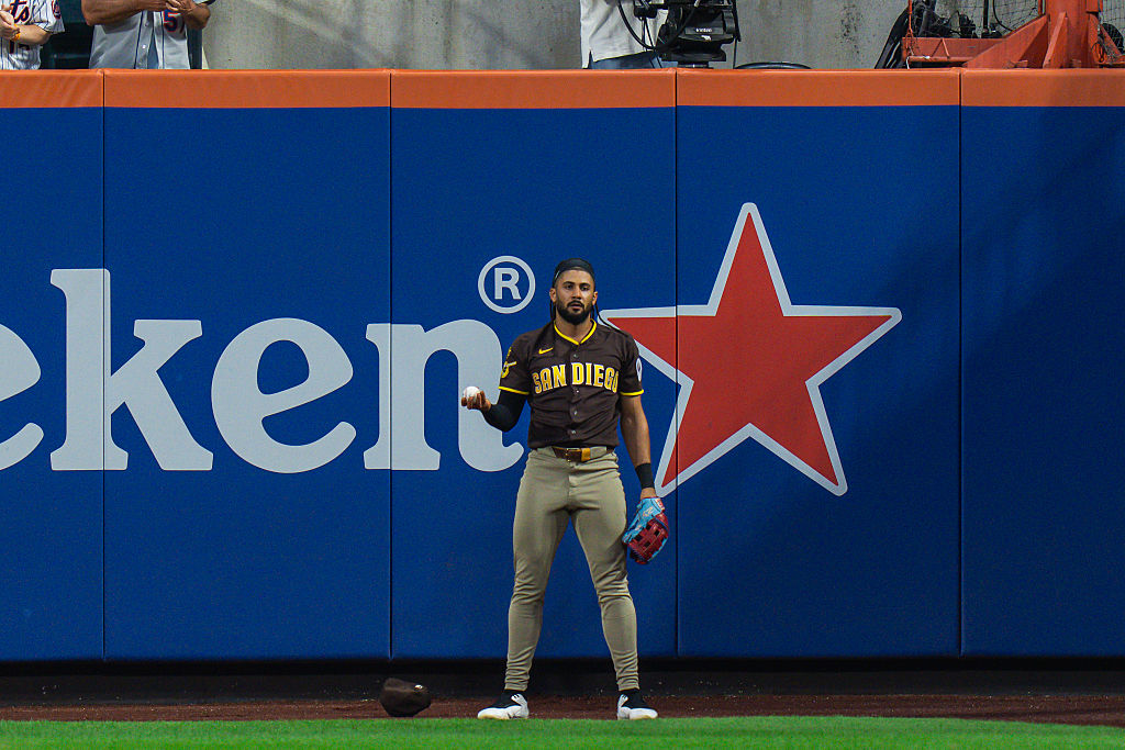 Fernando Tatis Jr. in a brown padres jersey, holds a ball flat in his right hand