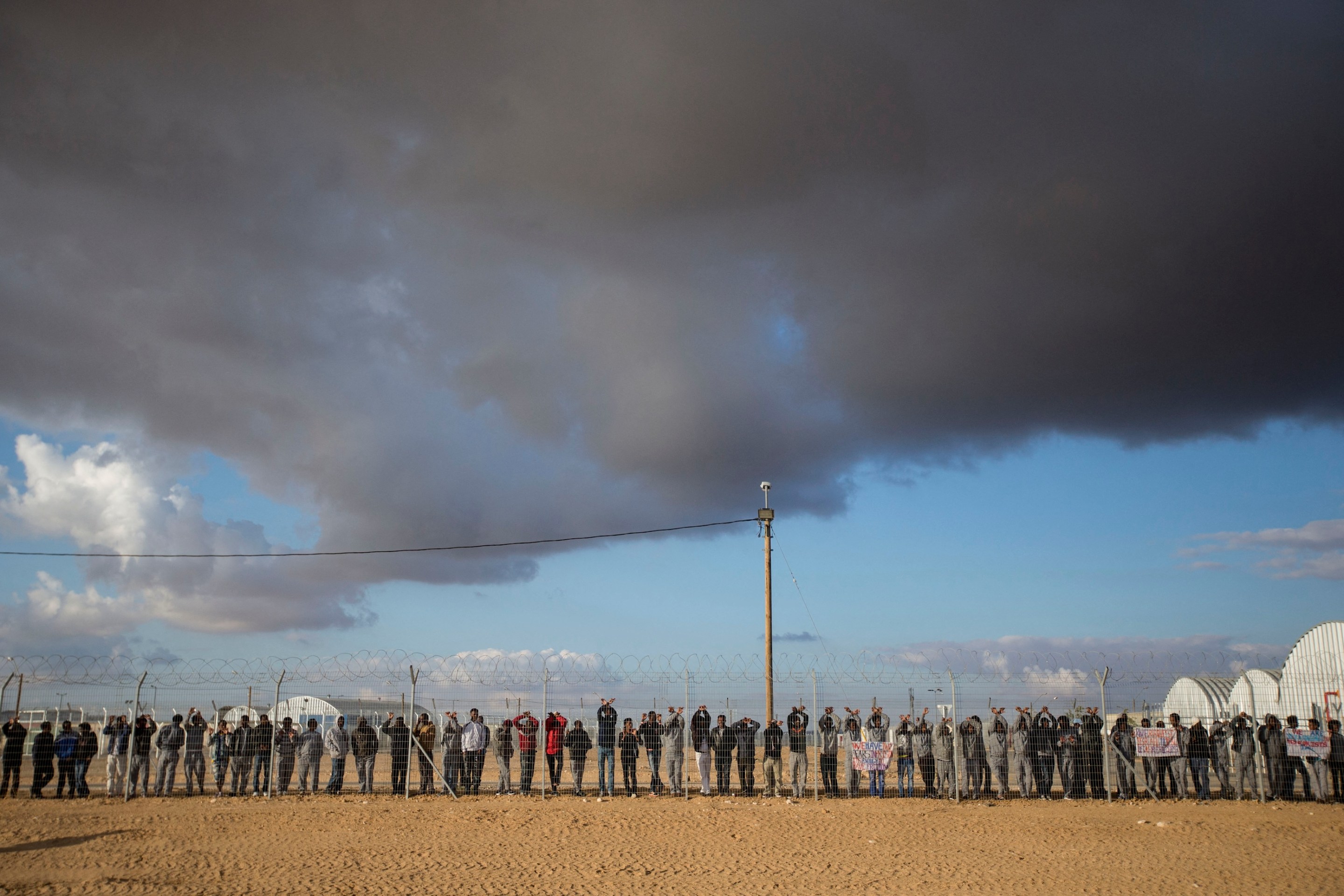 Asylum seekers, who entered Israel illegally via Egypt, lean at the fence of the Holot detention centre in Israel's southern Negev Desert, on February 17, 2014.