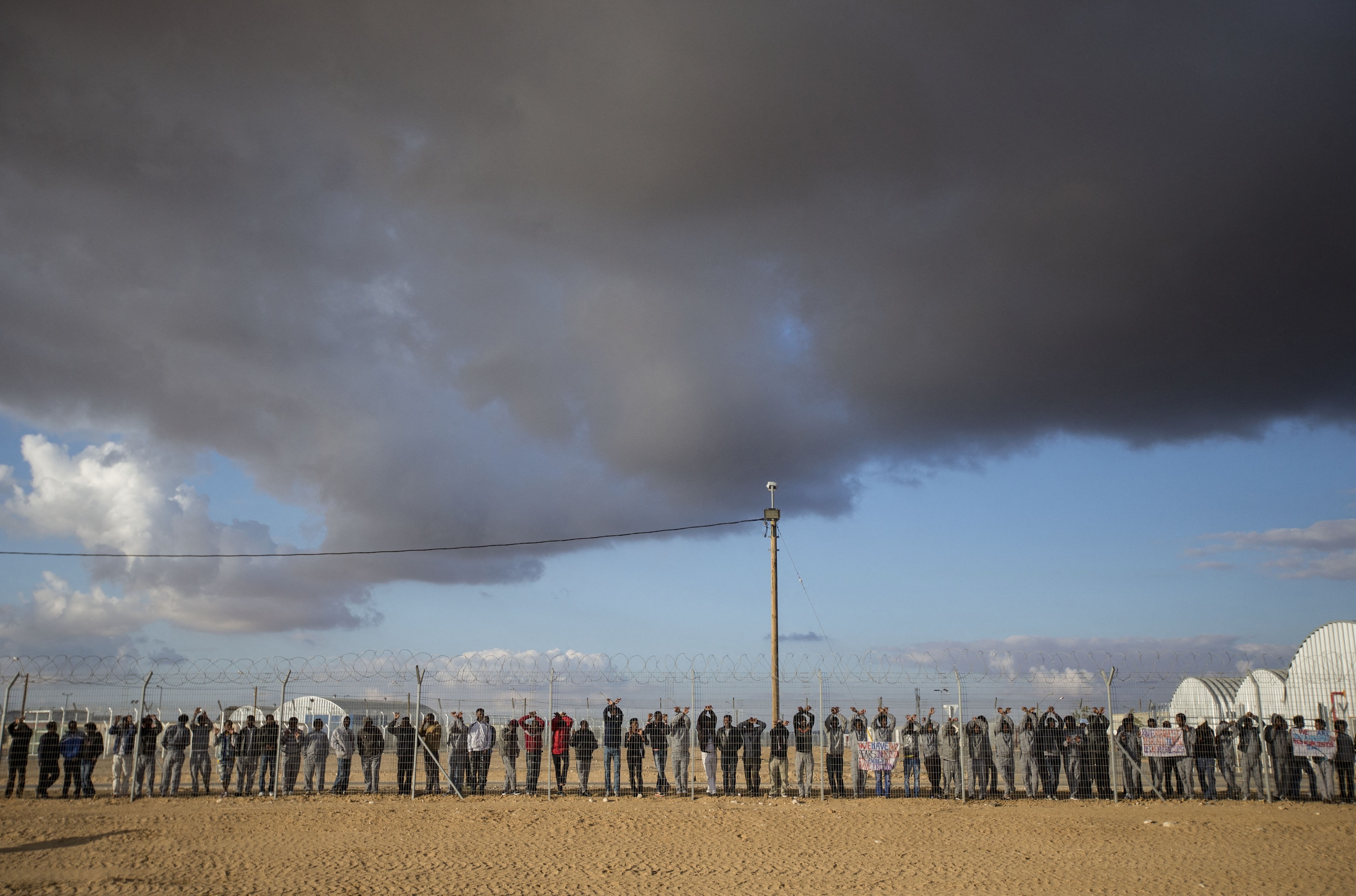Asylum seekers, who entered Israel illegally via Egypt, lean at the fence of the Holot detention centre in Israel's southern Negev Desert, on February 17, 2014.