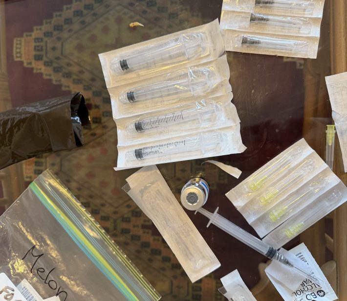 needles, syringes, and a vial of medicine on a glass table