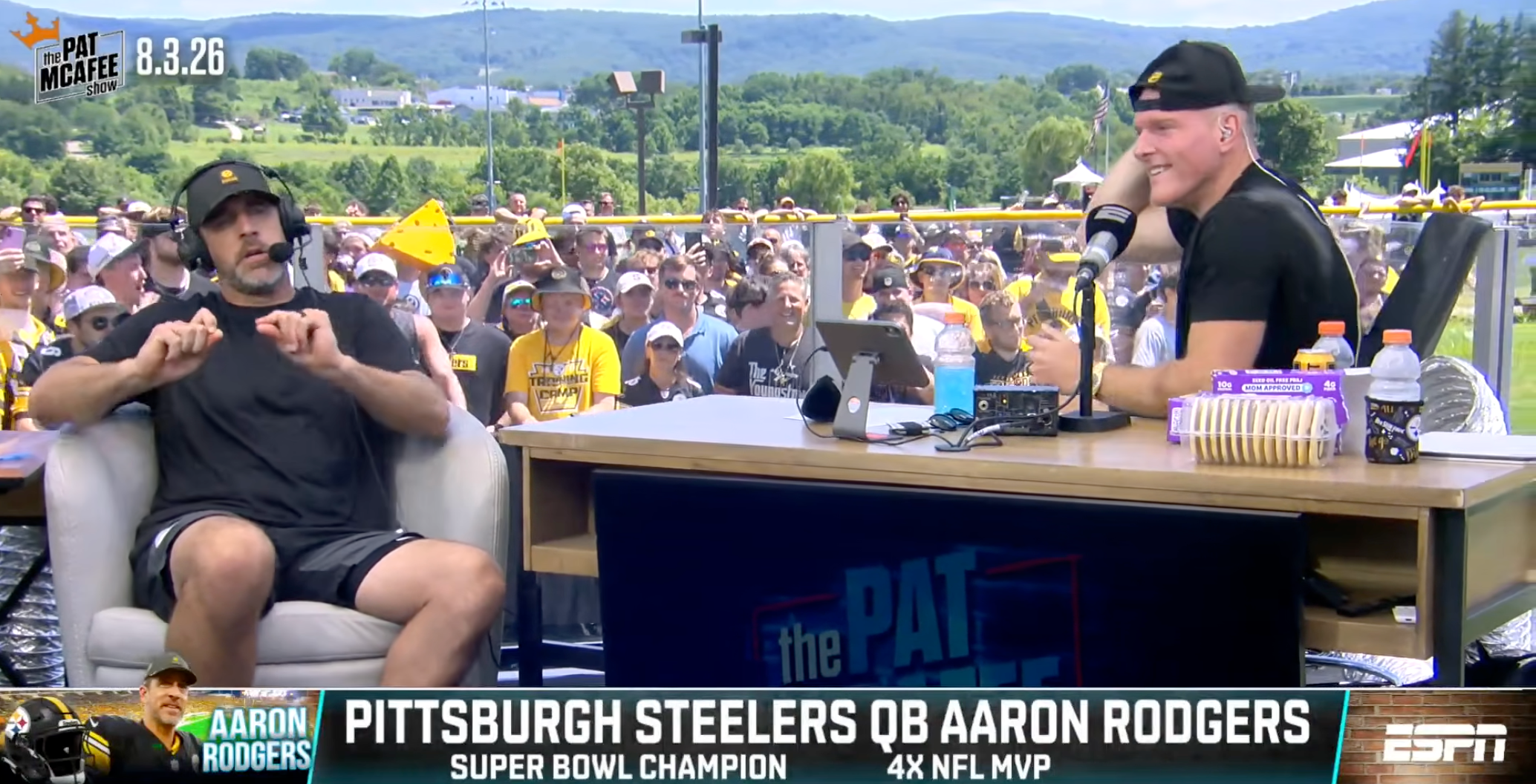 Aaron Rodgers being unbearable during an interview with Pat McAfee in front of a bunch of Steelers fans at training camp. McAfee looks pink and kind of boiled; Rodgers is slouching and pinching his fingers together.