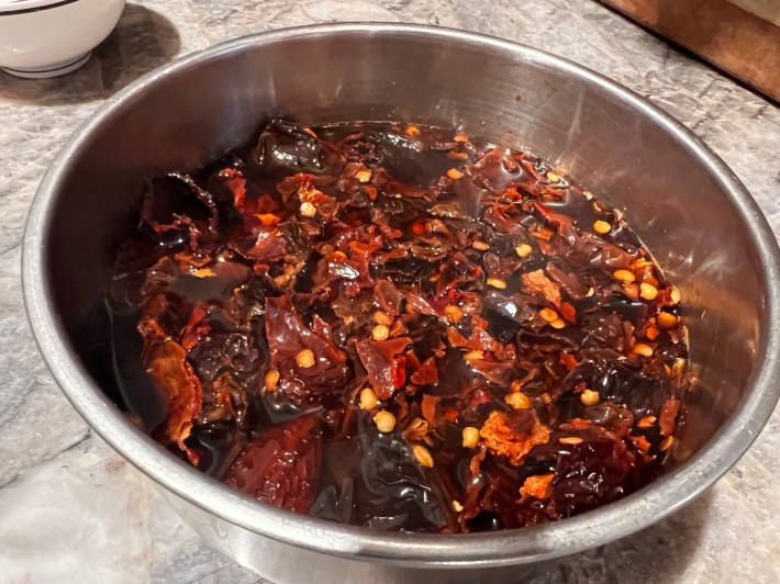 Chopped ancho chiles stew in very hot water, in a metal bowl.