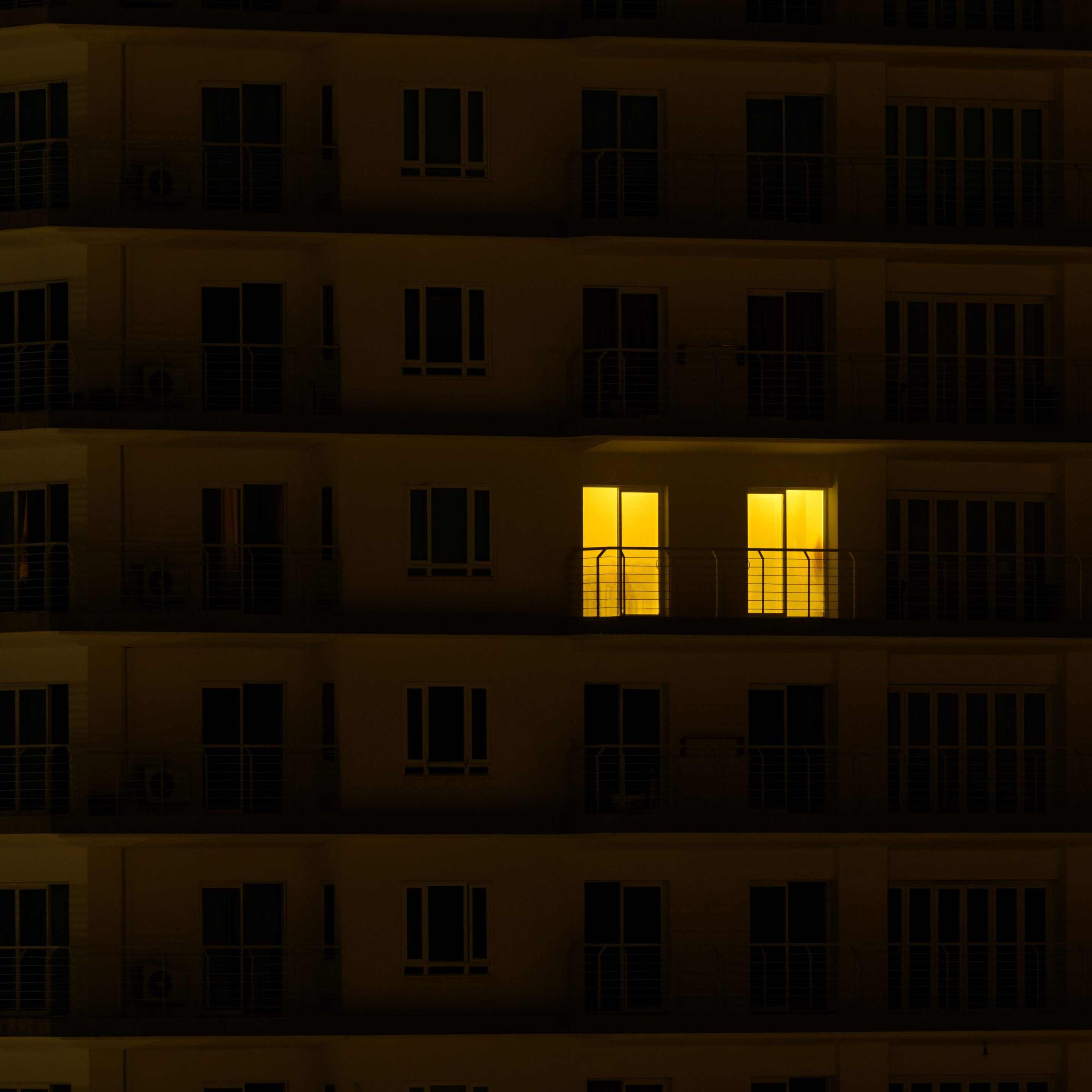 An apartment building where all the windows are blacked out except for two.