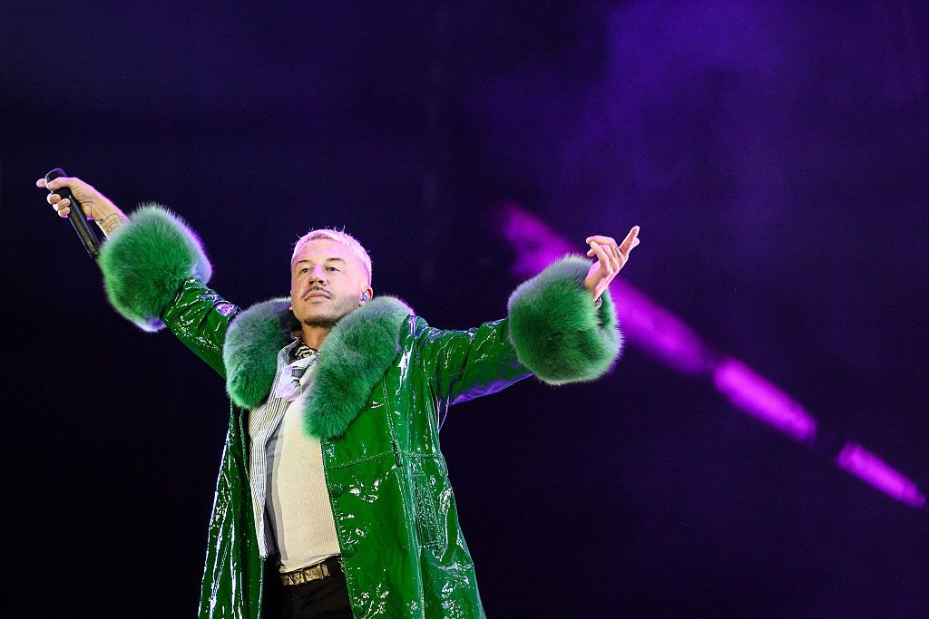 Macklemore in a green fur coat poses on stage.
