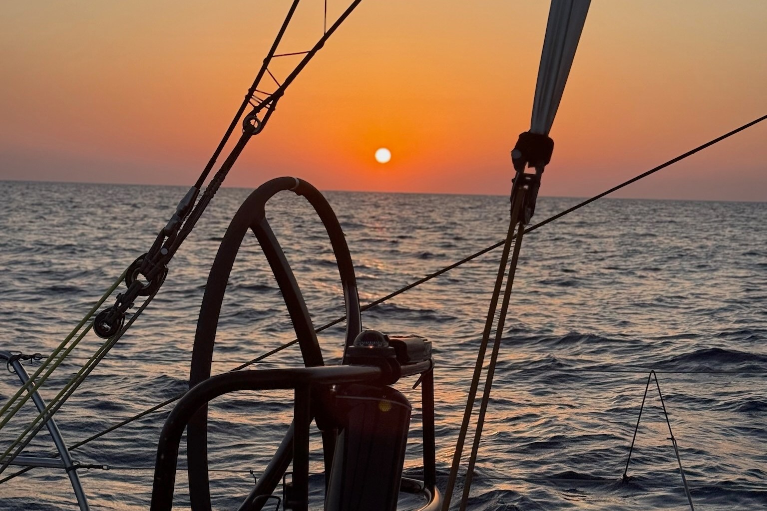 The sun setting behind a view of the boat's starboard helm, which is unoccupied.