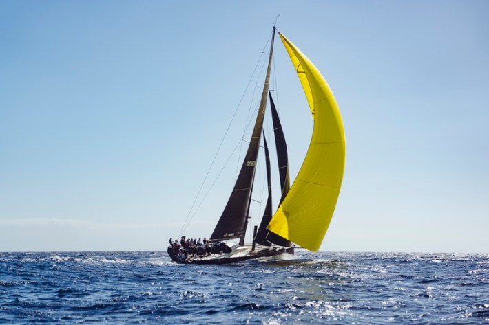 A promotional photo of Sisi, with a full crew, sailing with four sails, including a huge yellow downwind sail.