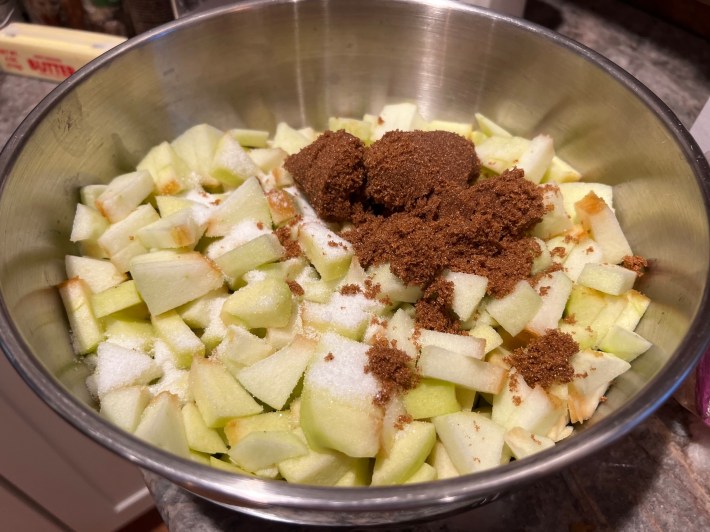 Chopped apples in a mixing bowl with granulated and brown sugars.