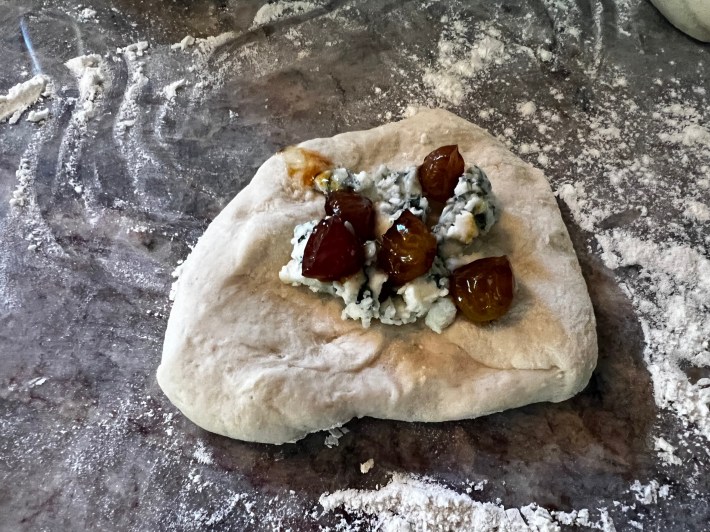 Blue cheese and roasted grapes on a circle of raw dough.