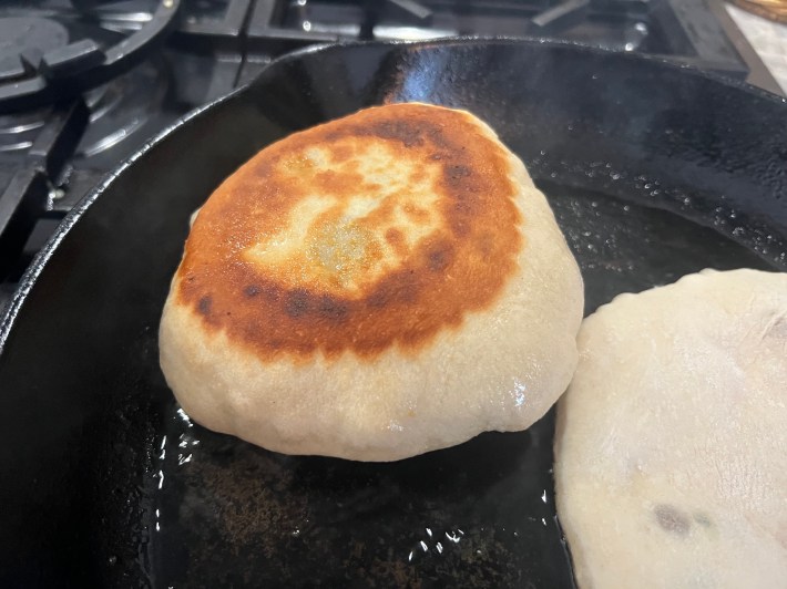 Flatbread dough is puffed up in a cast iron pan.