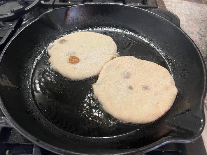 Two circles of dough are frying in a cast iron pan