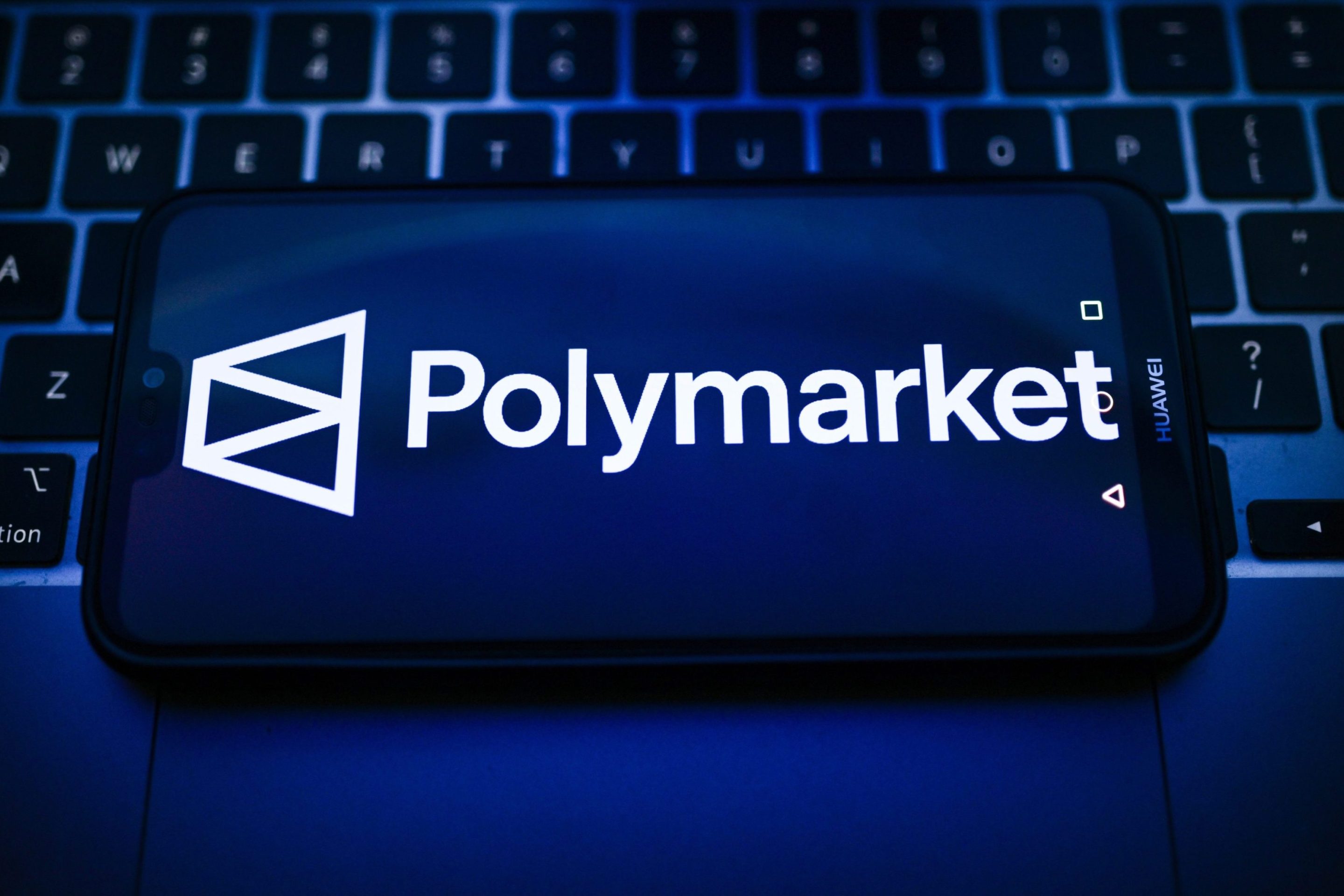 In this photo illustration, a Polymarket logo is seen displayed on a smartphone on the top of a laptop.