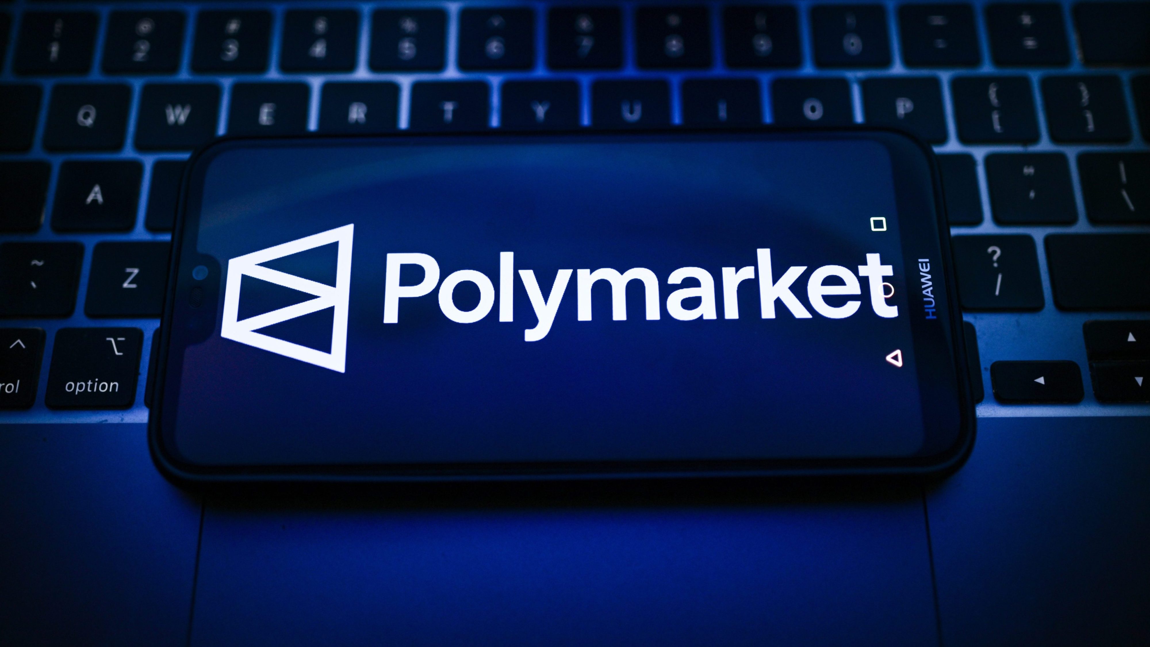 In this photo illustration, a Polymarket logo is seen displayed on a smartphone on the top of a laptop.