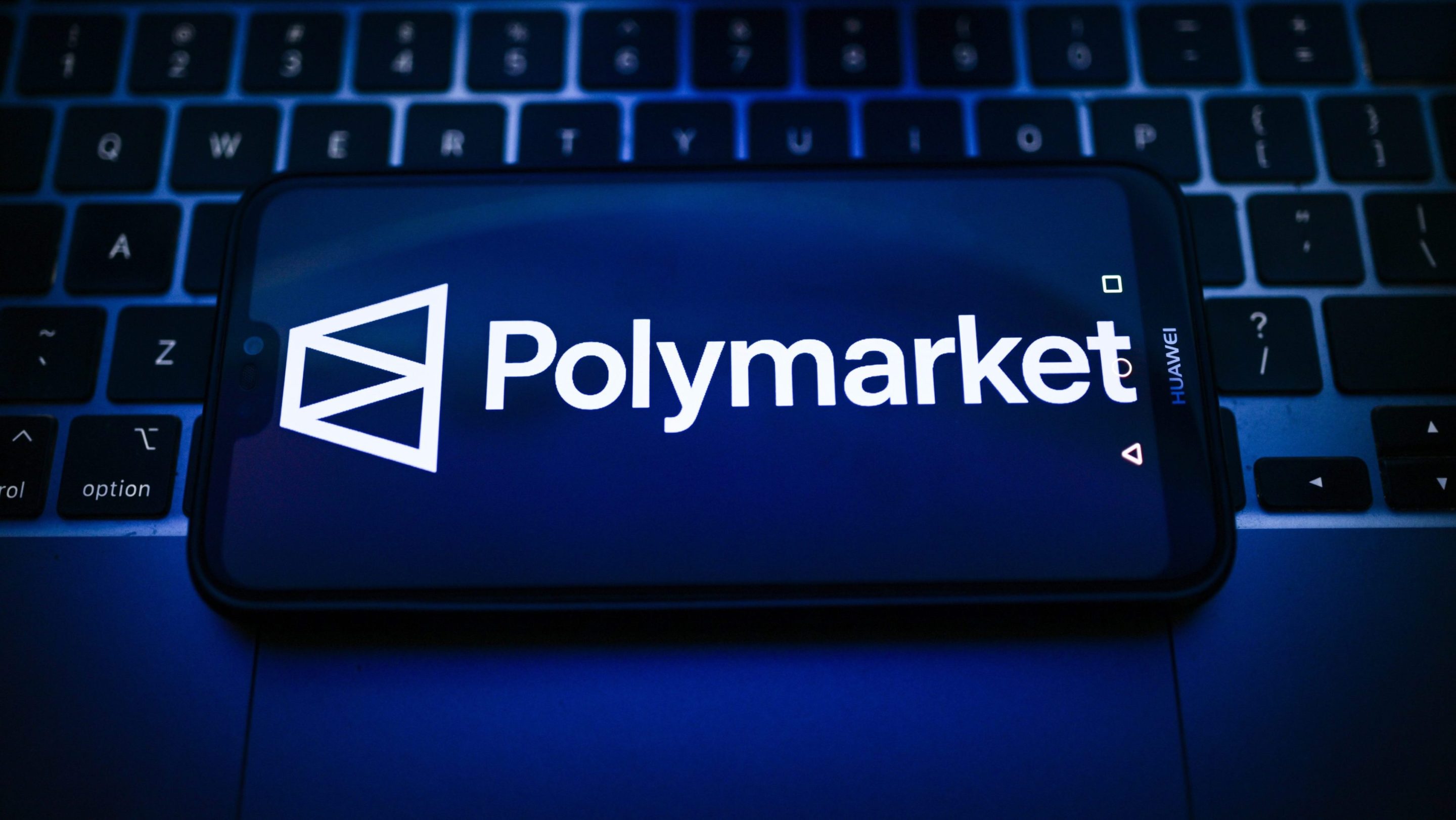 In this photo illustration, a Polymarket logo is seen displayed on a smartphone on the top of a laptop.