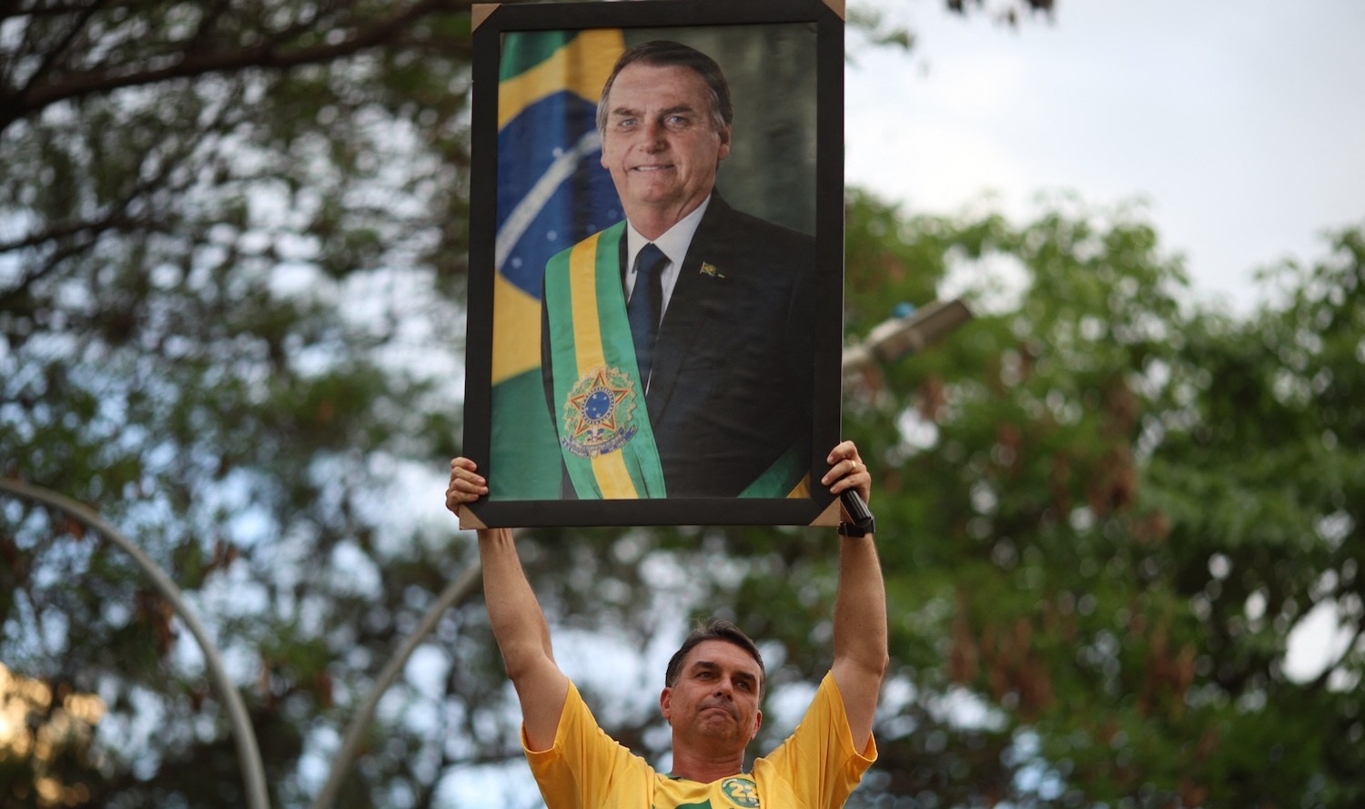 Brazilian right-wing presidential candidate Flavio Bolsonaro holds a picture of his father, convicted former President Jair Bolsonaro, during a motorcade with supporters in Goiania, Brazil, on September 27, 2026. Brazil will hold presidential election on October 4, 2026. (Photo by Sergio Lima / AFP)