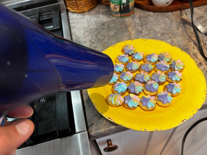A blue hair dryer blowing onto 24 iced shortbread cookies.