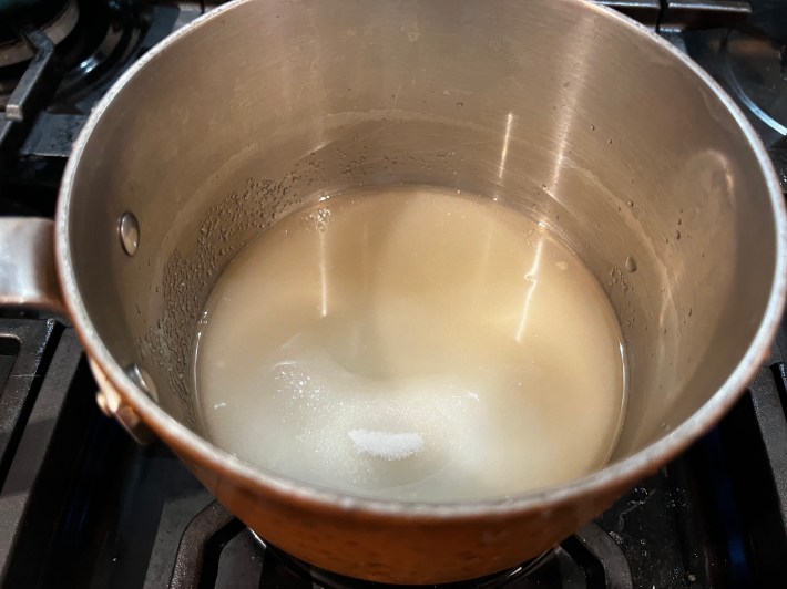 Granulated sugar and apple cider cook inside a saucepan.
