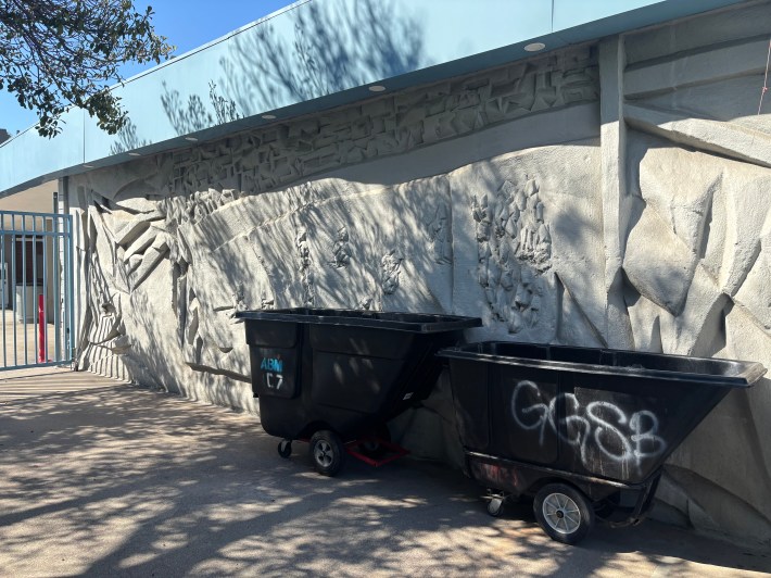 A color image of the Dodger Stadium's concrete murals, with some plastic dumpsters sitting there in front of them.