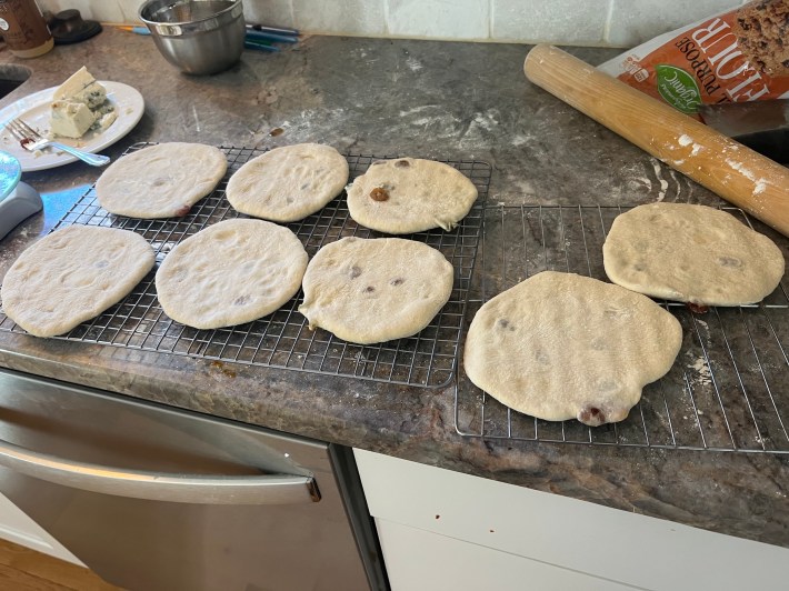 Eight circles of raw flatbread dough are lined up on cooling racks.