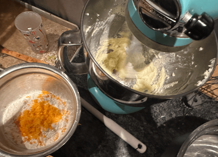 blue kitchenaid mixer with butter in it, bowl of flour and orange zest.