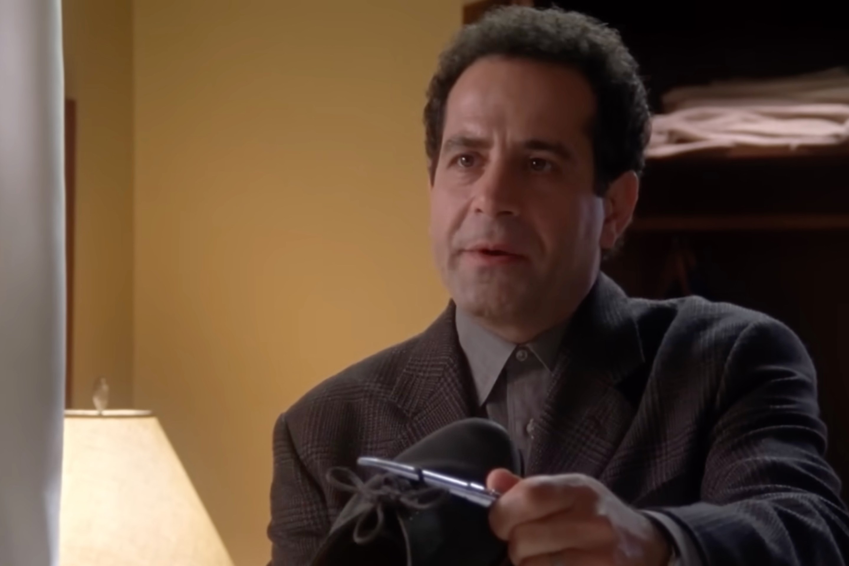 Tony Shalhoub as Adrian Monk holding up a shoe with a pen