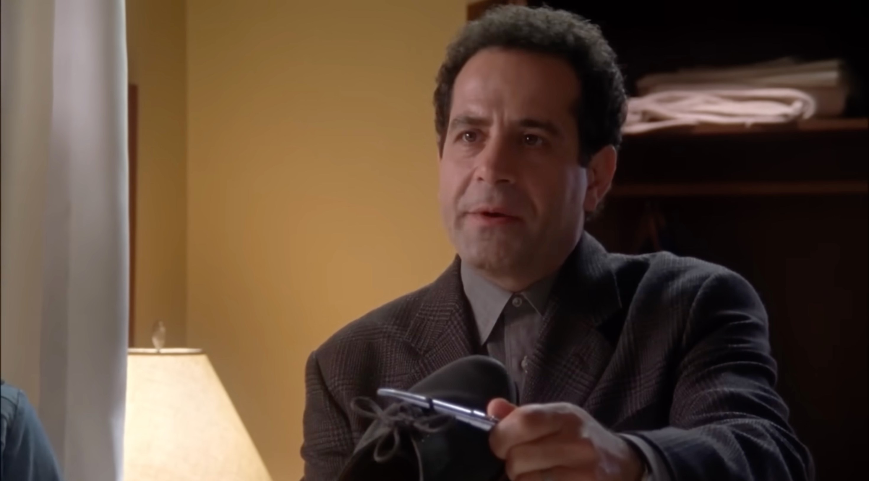 Tony Shalhoub as Adrian Monk holding up a shoe with a pen